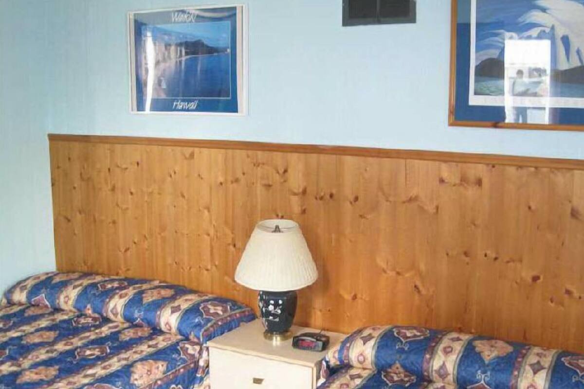 A bedroom with a wooden headboard, two patterned beds, a nightstand with a lamp, and framed pictures on the wall.