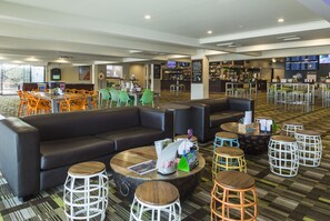 A modern lounge area with a sofa, round tables, and bar stools. - Nightcap at Edge Hill Tavern (Manoora)