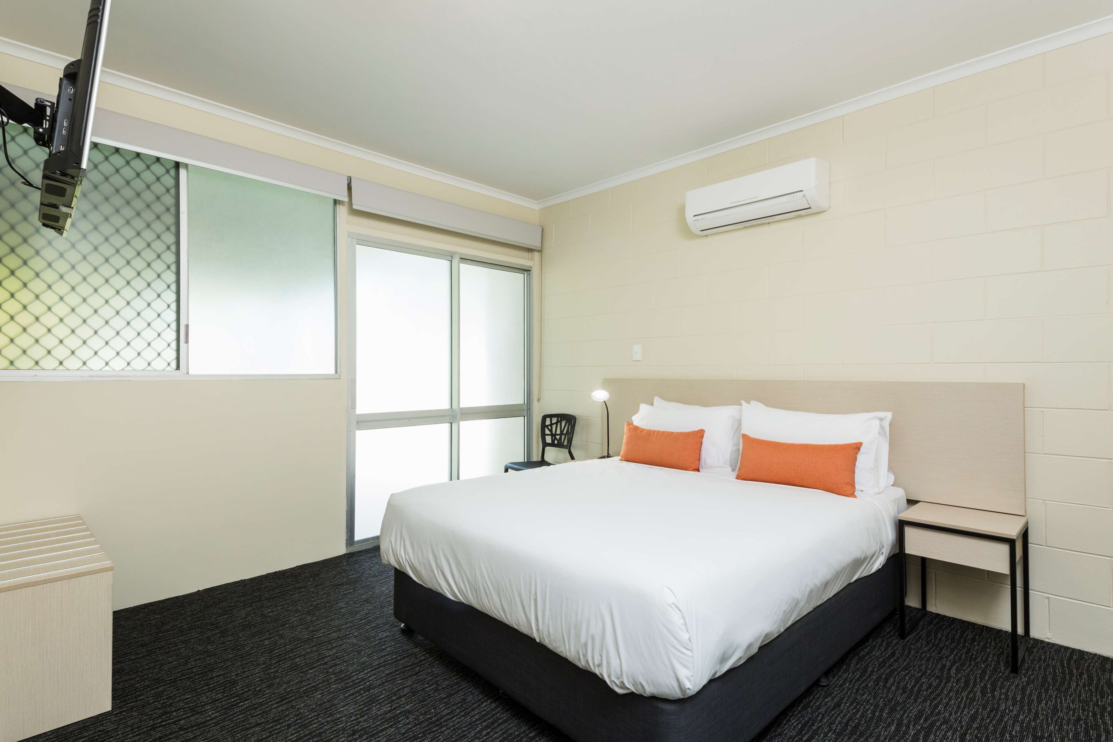 A hotel room with a large bed, a nightstand, a chair, and a window with blinds.