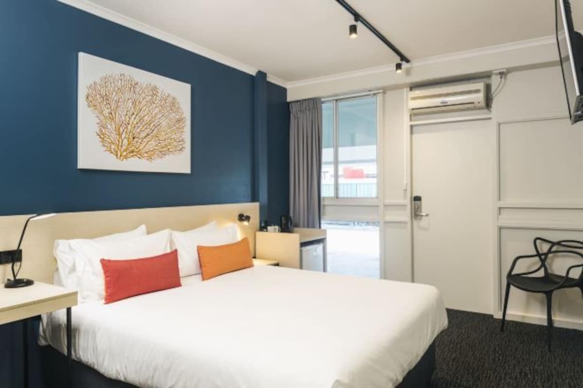 Una habitación de hotel con cama, escritorio, silla y ventana con cortinas.