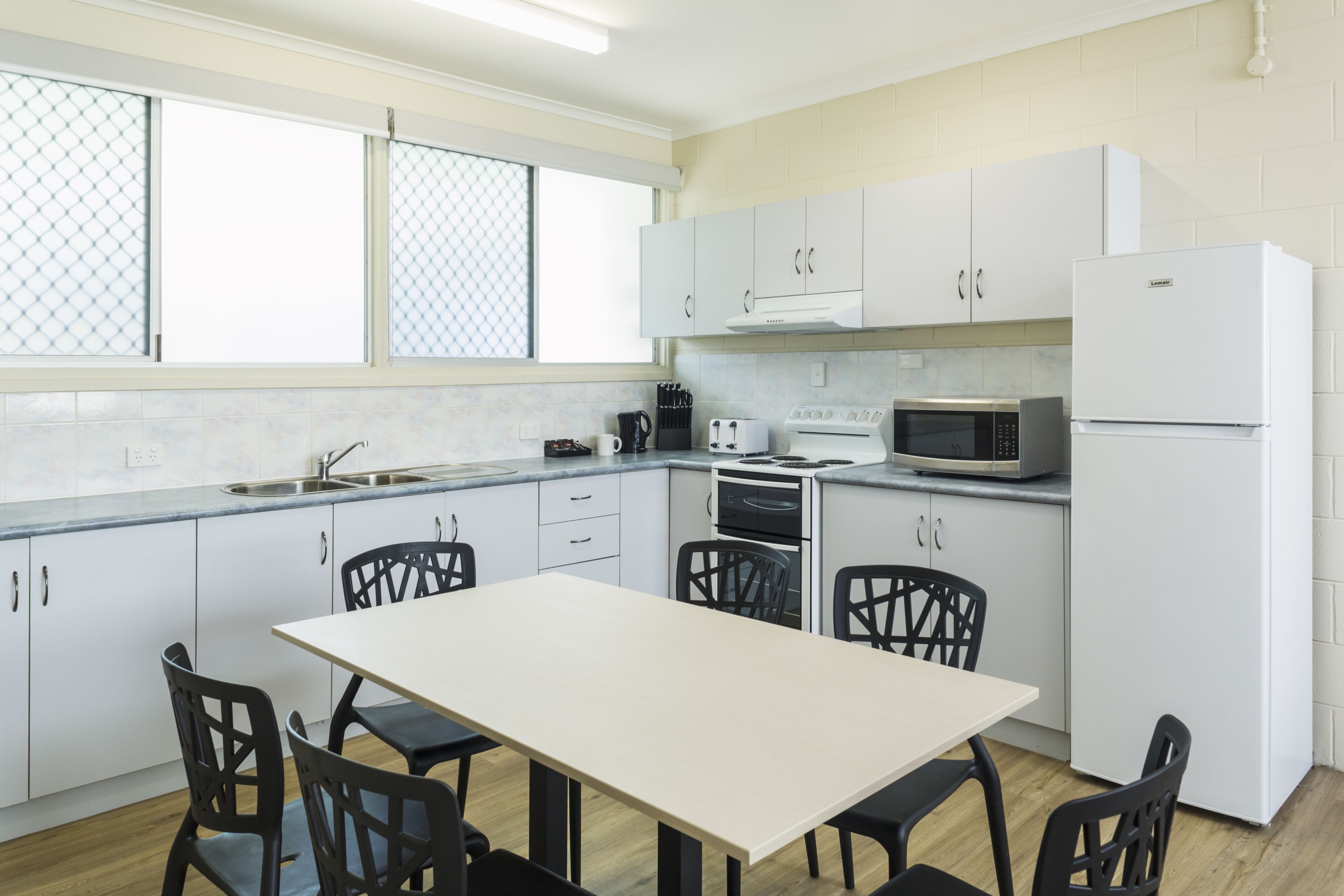 A modern kitchen with white cabinets, a dining table with chairs, a microwave, an oven, and a refrigerator.