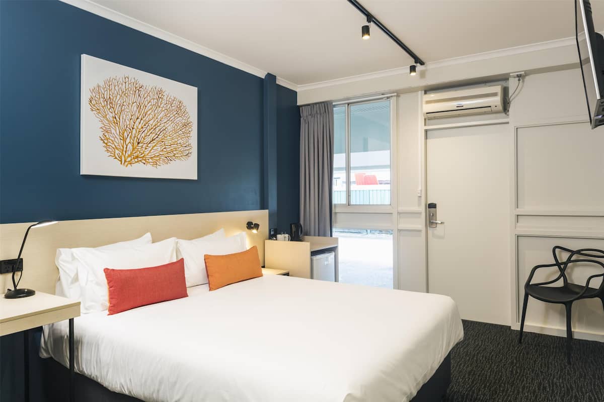 Quarto de hotel com cama, escrivaninha, cadeira, ar condicionado fixado na parede e janela com cortinas.