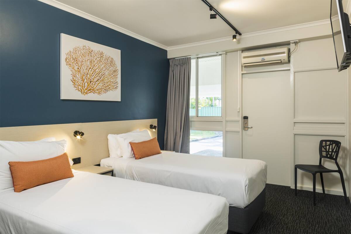 Quarto de hotel com duas camas, um ventilador de teto, uma janela com cortinas e um ar condicionado fixado na parede.