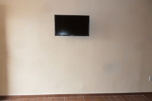 A room with a flat-screen TV mounted on the wall, a tiled floor, and a plain wall. - Motel 6 Blythe, CA - South (Blythe)