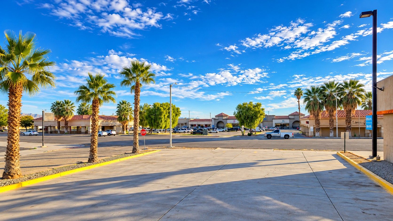 A parking lot with palm trees, a stop sign, and buildings in the background.