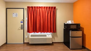 A hotel room with a door, an air conditioning unit, a refrigerator, and a microwave on a counter. - Motel 6 Blythe, CA - South (Blythe)