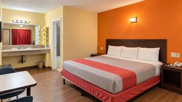 Et hotelværelse med seng, skrivebord, spejl og et badeværelse, der ses gennem en åben dør.