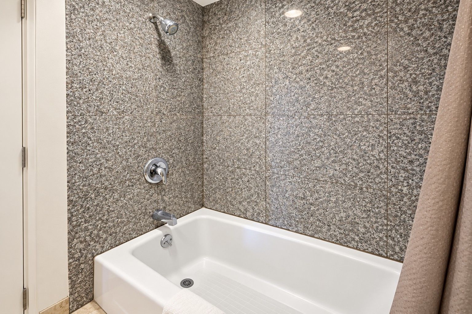 A bathroom with a white bathtub, a showerhead, and a wall with speckled tiles.