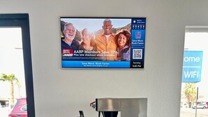Una estación de café con cafetera, dispensadores de azúcar y crema, y un cartel publicitando los beneficios para miembros de AARP.