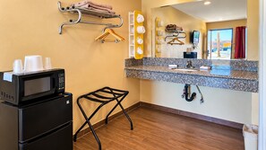 A compact hotel room with a kitchenette, a small stool, a towel rack, and a mirror with a view of the outside. - Motel 6 Blythe, CA - South (Blythe)