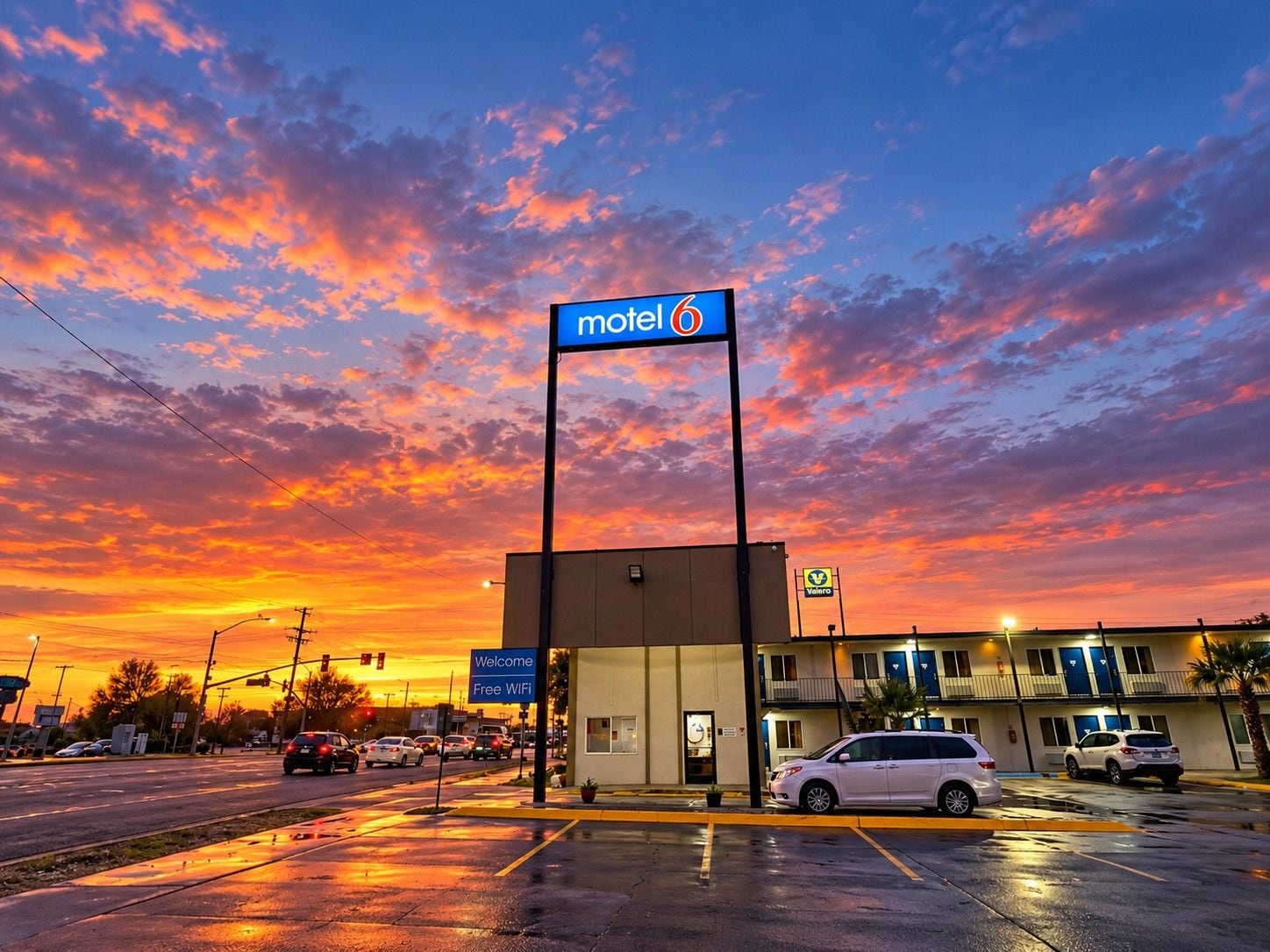 A motel with a sign indicating free WiFi, a parking lot with cars, and a sunset sky.
