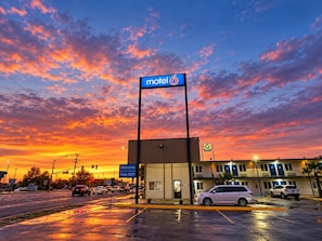 A motel with a sign indicating free WiFi, a parking lot with cars, and a sunset sky. - Motel 6 Blythe, CA - South (Blythe)