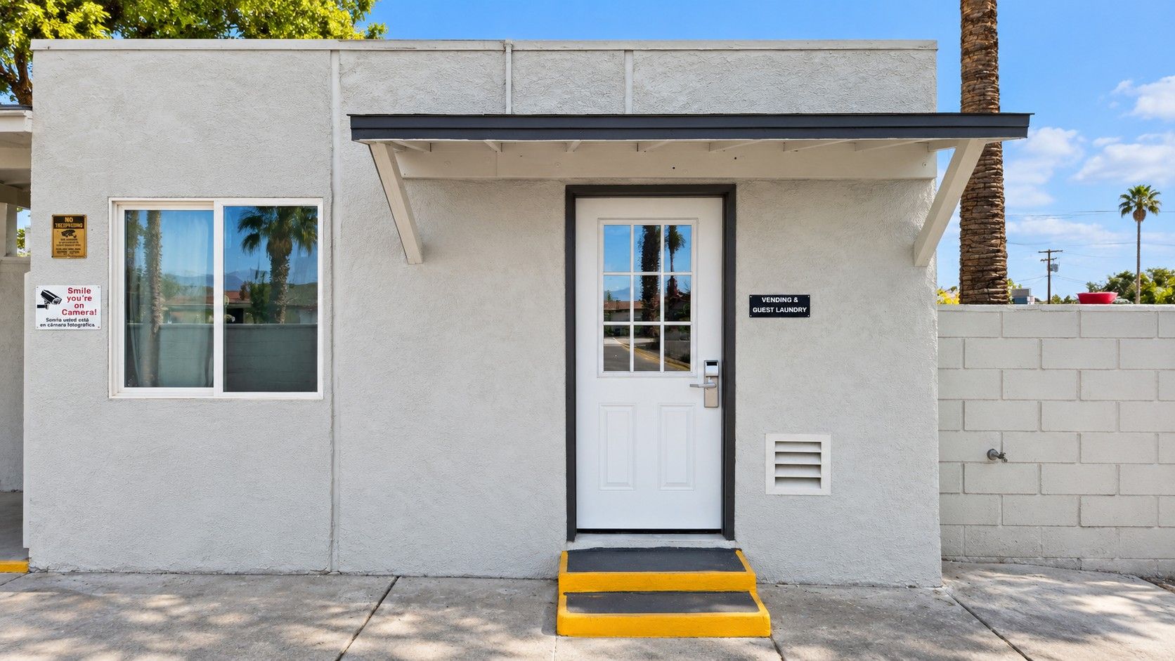 A small, single-story building with a white exterior, a black-framed door, and a yellow and black striped step leading to the entrance.