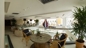 A modern indoor space with a round wooden table, wicker chairs, and a large potted plant. - Hotel French Ipoh (Ipoh)