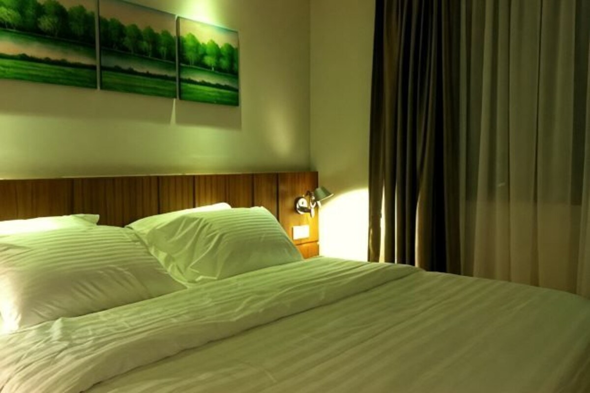 A hotel room with a bed, a nightstand, a lamp, and a painting on the wall.