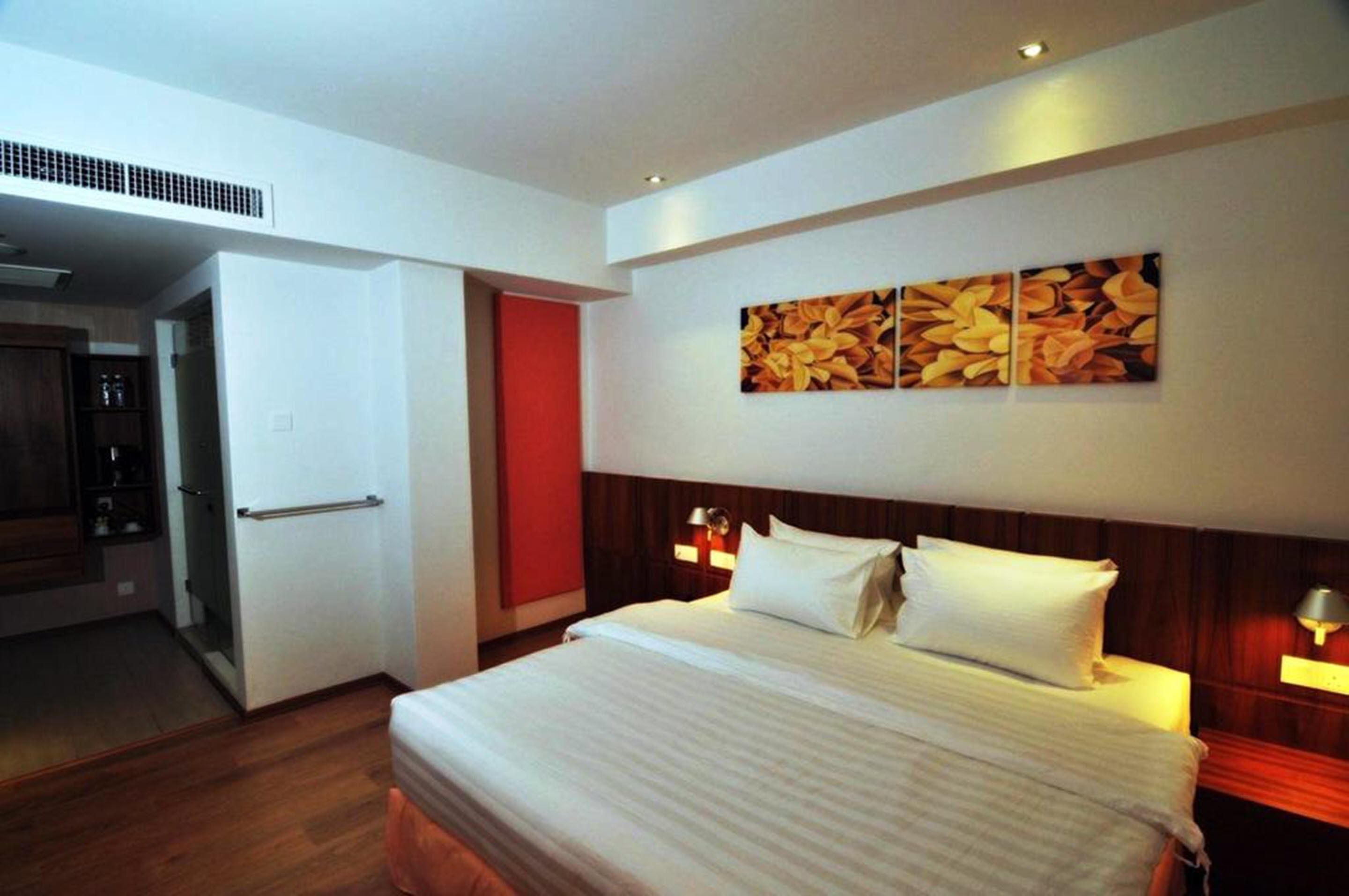 Une chambre d’hôtel avec un lit, une porte rouge et un mur orné de trois œuvres d’art encadrées.