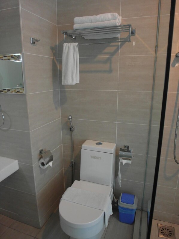 A modern bathroom with a toilet, a glass shower enclosure, a towel rack, and a trash bin. - Hotel French Ipoh (Ipoh)