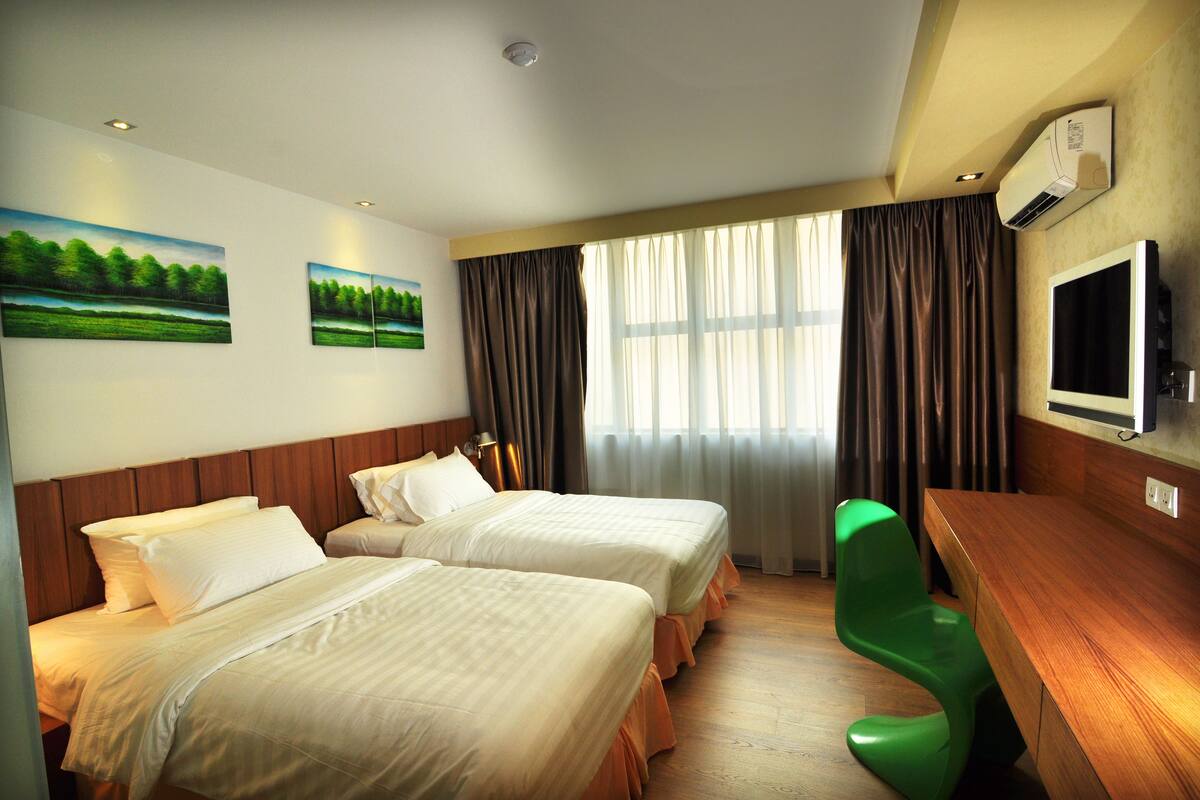 A hotel room with two beds, a wooden desk, a television, and a window with curtains.