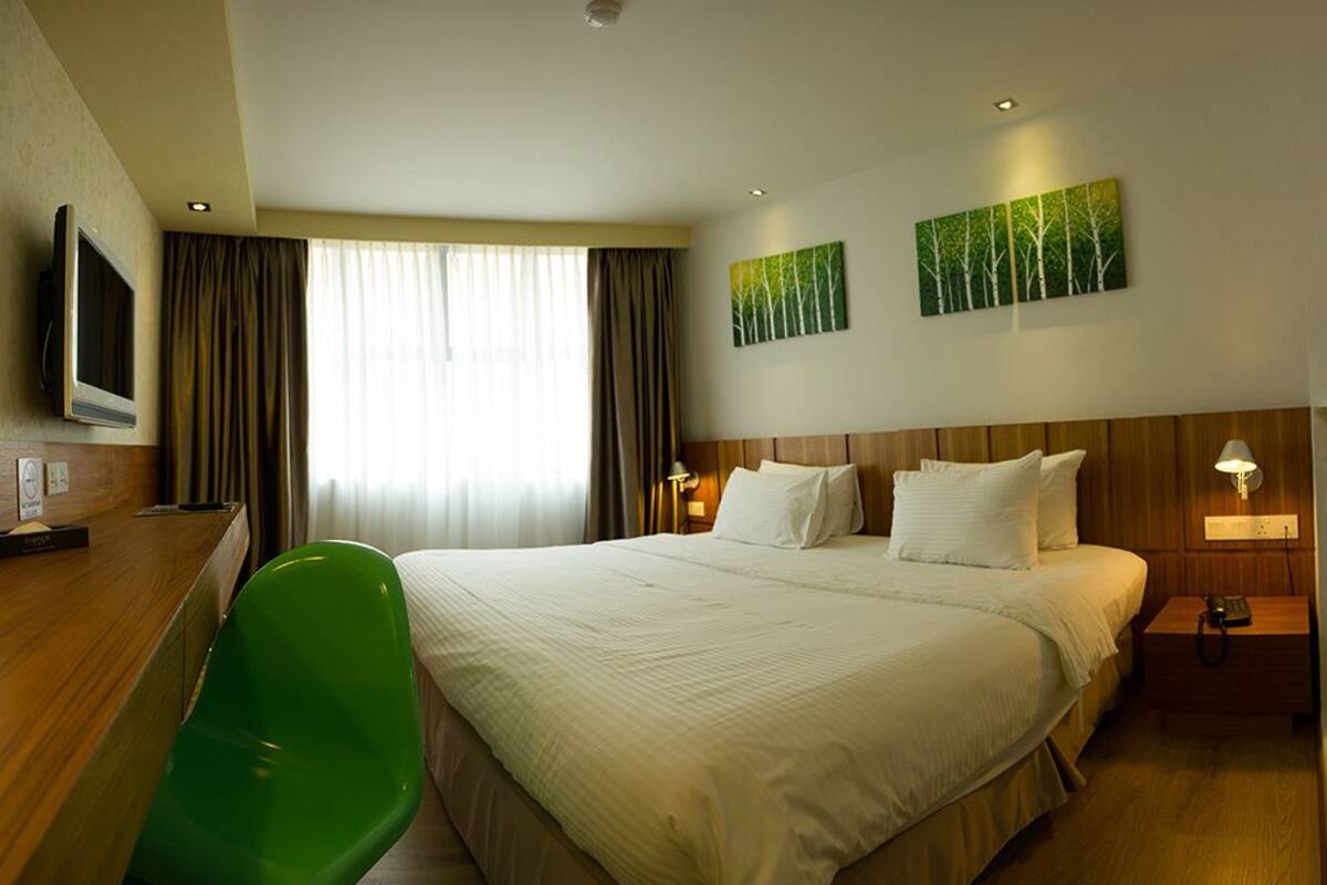 A hotel room with a large bed, a desk with a chair, a television, and two paintings on the wall.