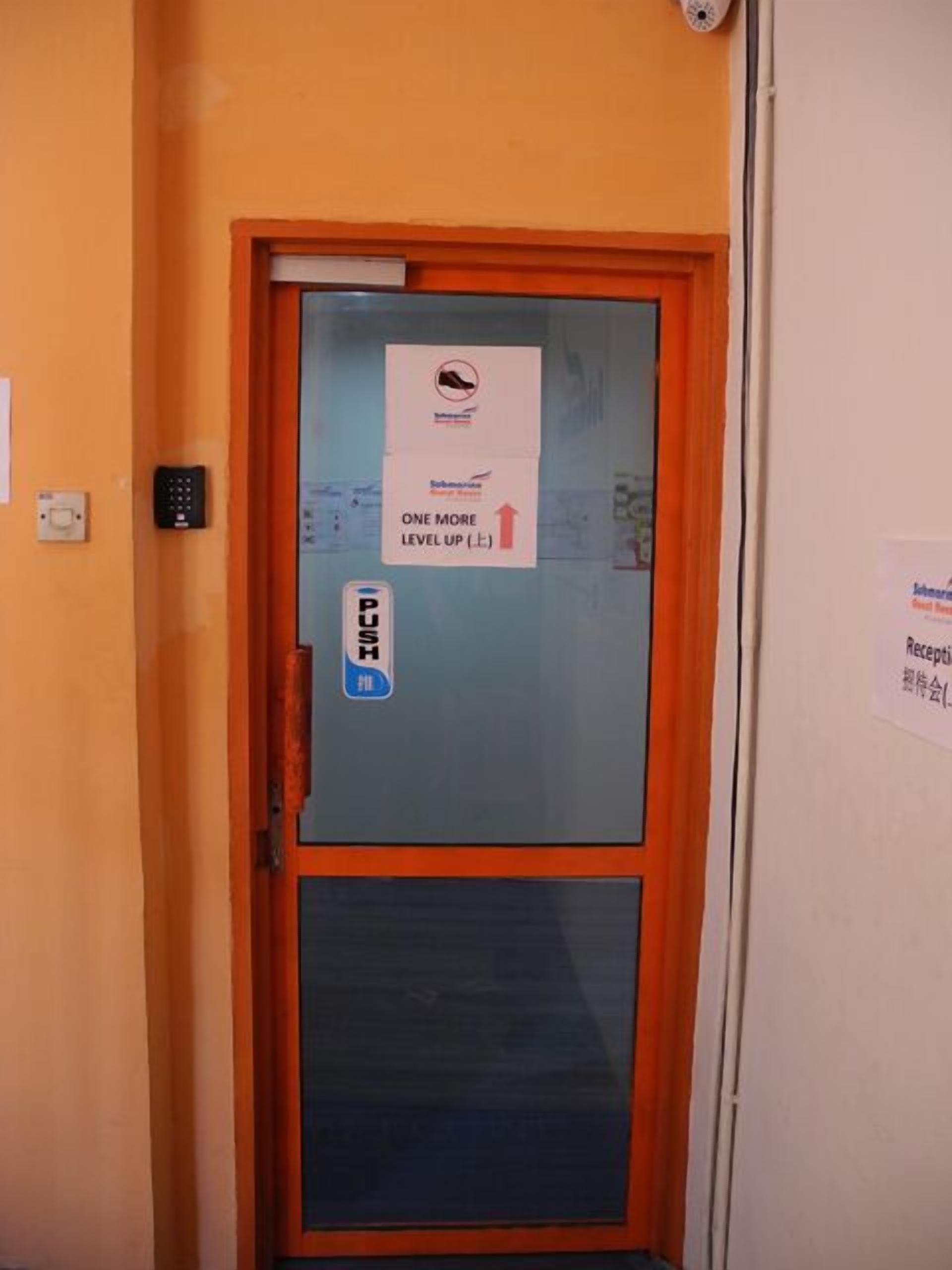 Porta de quarto de hotel com uma placa indicando 'UM NÍVEL ACIMA' e um botão de 'ABRIR'.