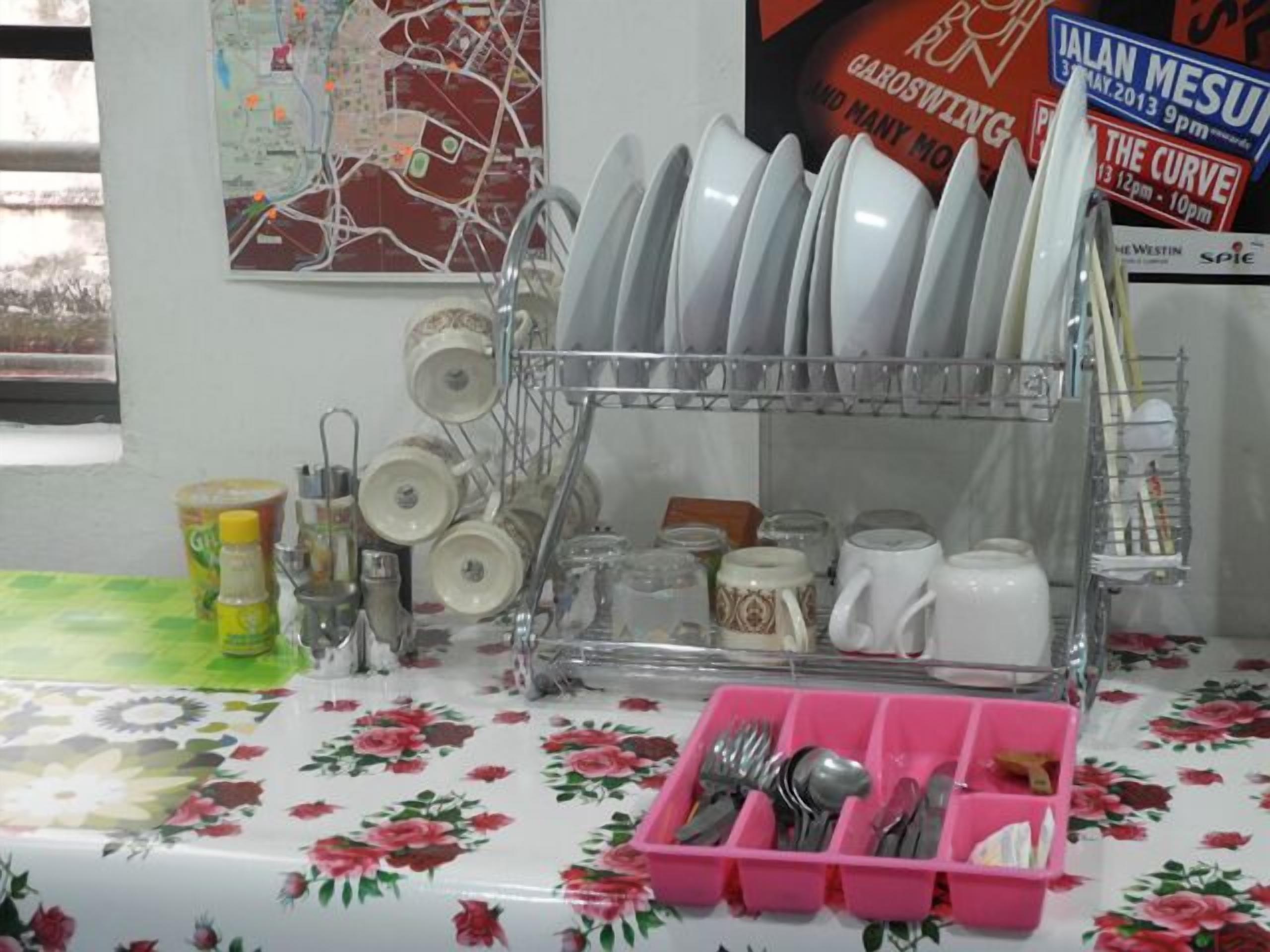 Uma área de cozinha com escorredor de louça contendo pratos e tigelas, um porta-utensílios rosa e um mapa na parede.