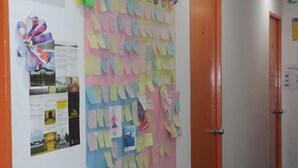 A hallway with a bulletin board covered in colorful notes and a 'No Smoking' sign. - Submarine Guest House Central Market - Hostel (Kuala Lumpur)