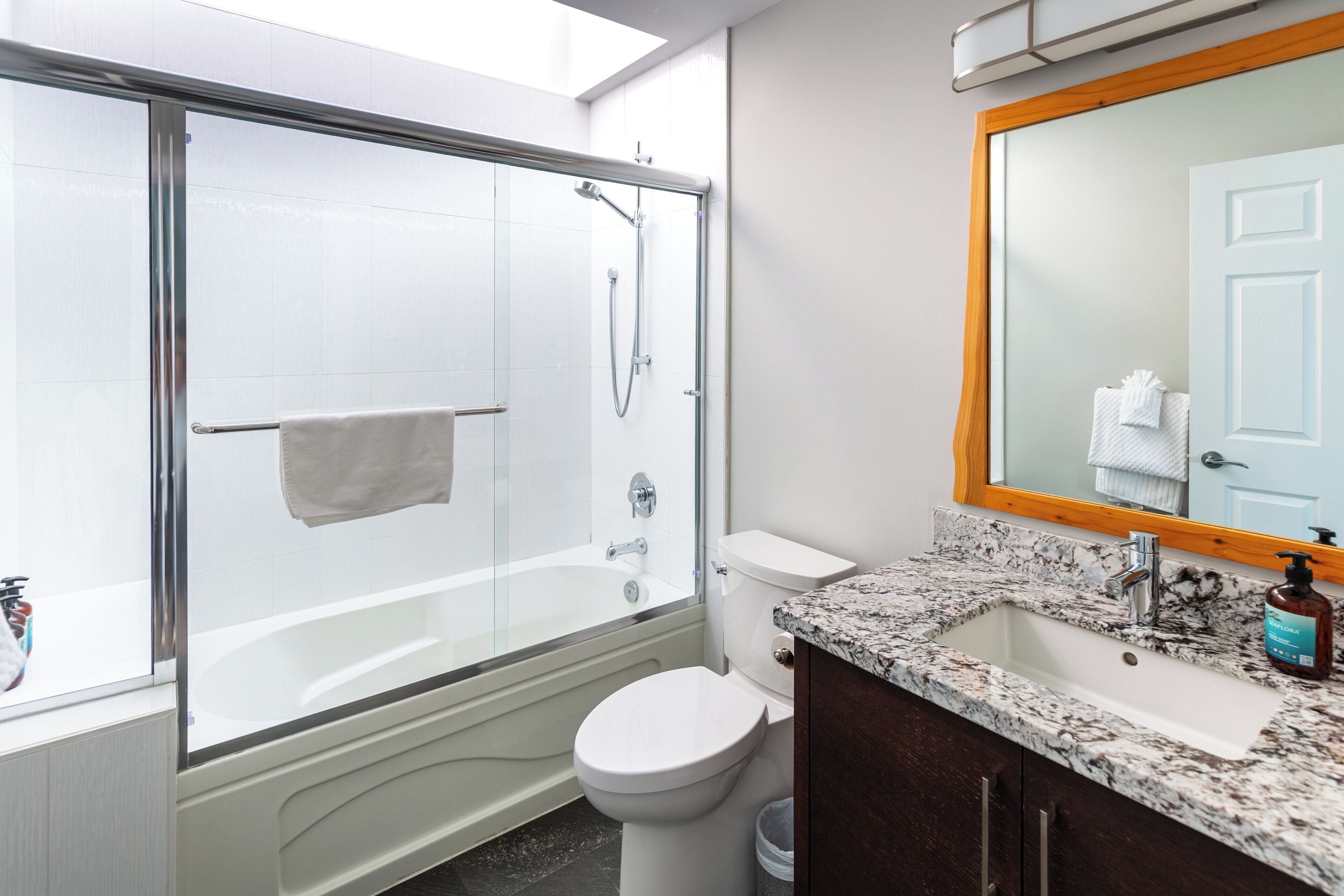 Un baño moderno con ducha de vidrio, inodoro blanco, lavamanos de mármol y un espejo grande.
