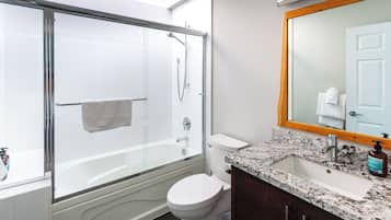 Un baño moderno con ducha de vidrio, inodoro blanco, lavamanos de mármol y un espejo grande.