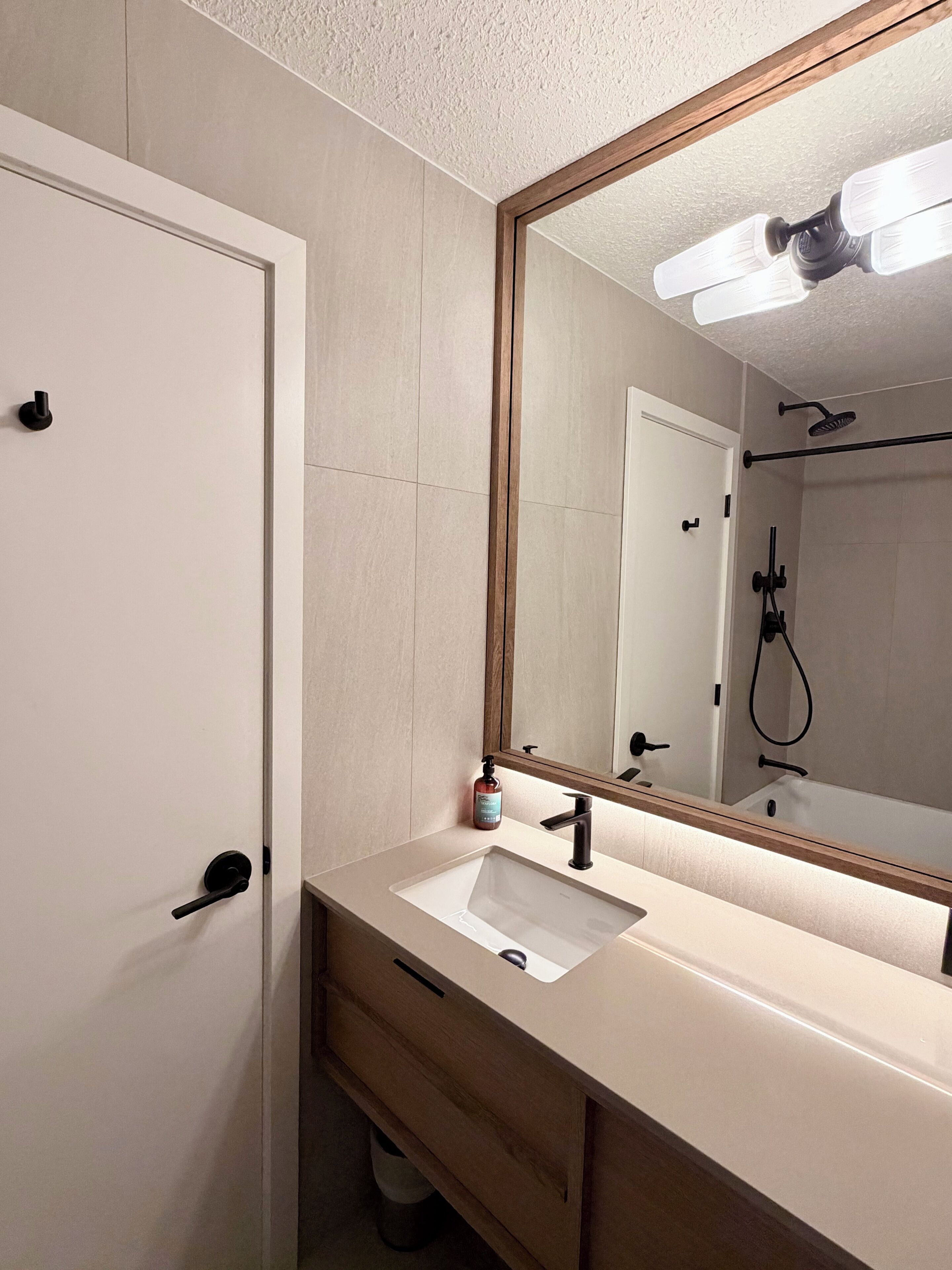 A bathroom with a white sink, a mirror, a shower, and a door.