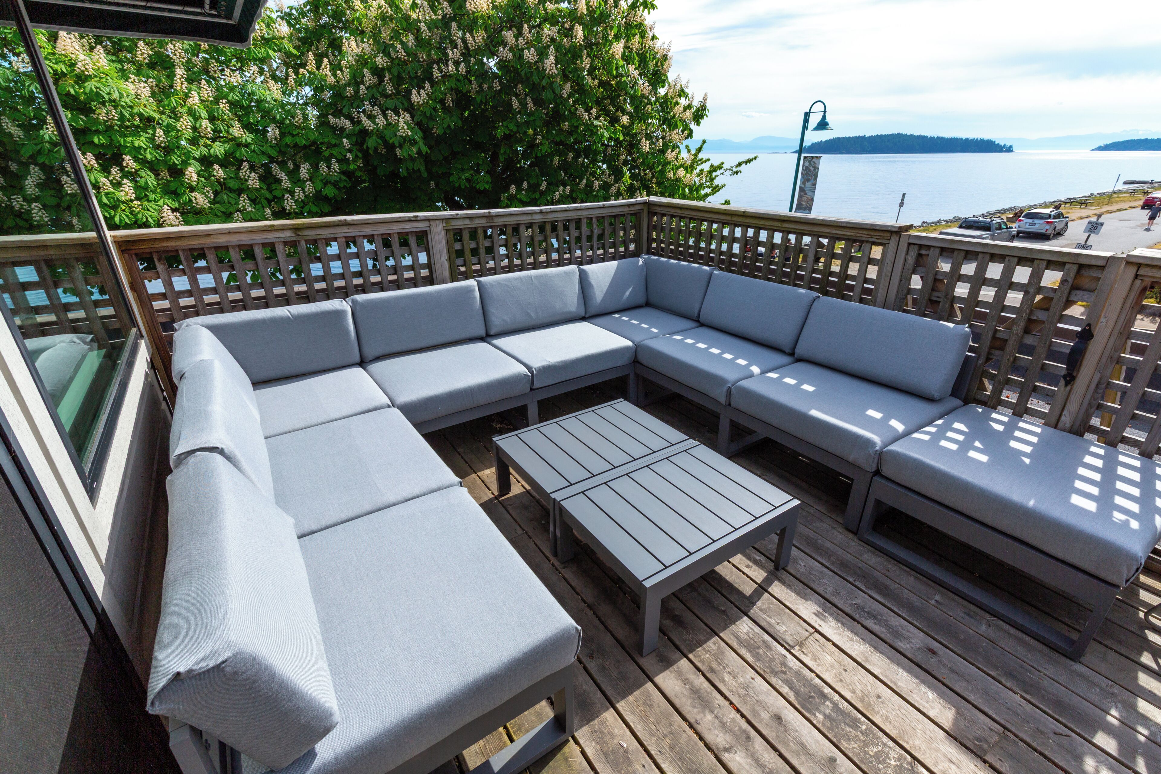 A deck with a gray sectional sofa, a small table, and a wooden railing.