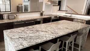 A modern kitchen with a large island, bar stools, stainless steel appliances, and a view of the outdoors. - Sechelt Inn (Sechelt)