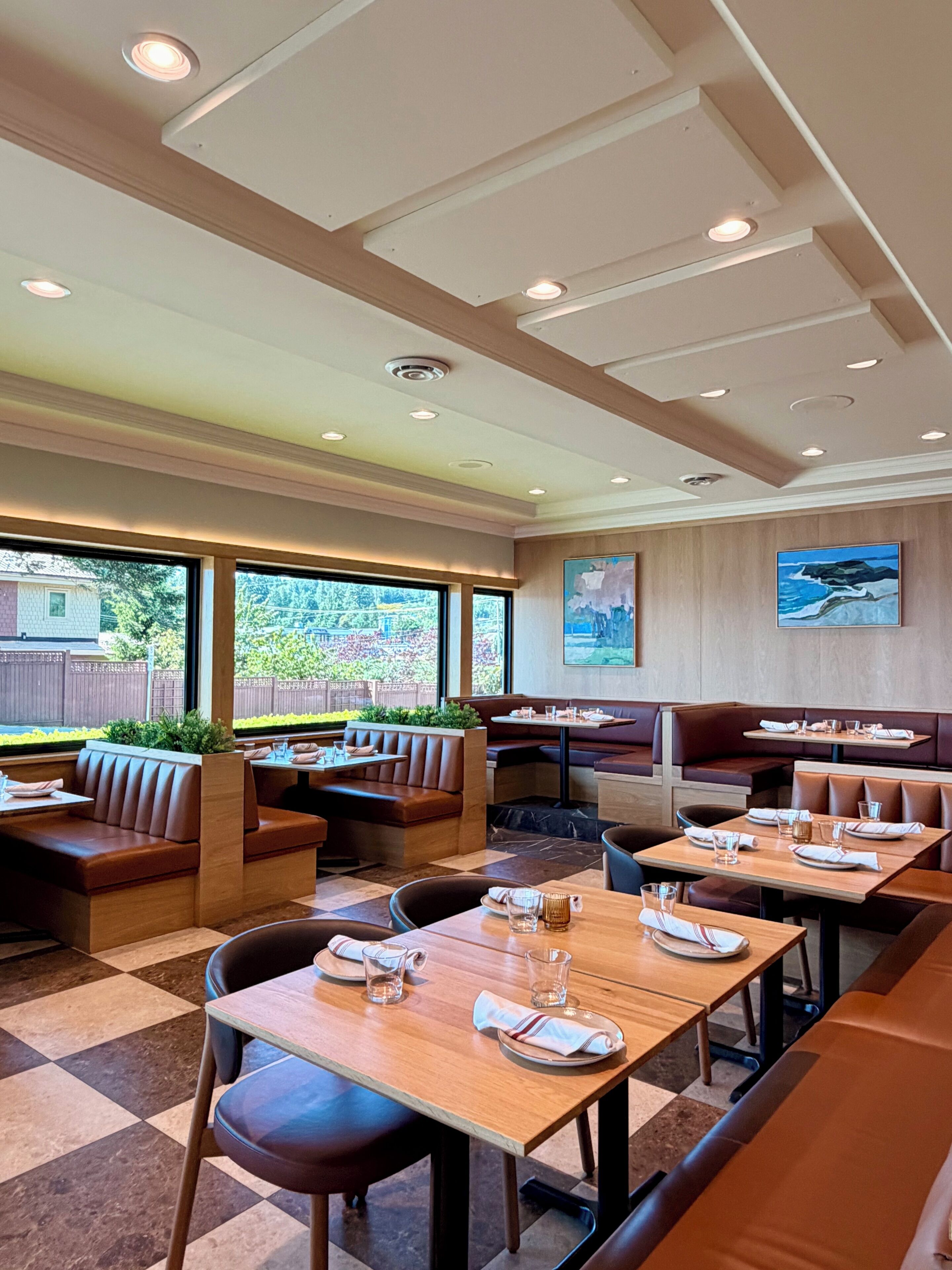 A restaurant with booths and tables, large windows, and a view of greenery.