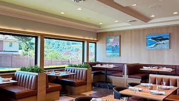 A restaurant with booths and tables, large windows, and a view of greenery.