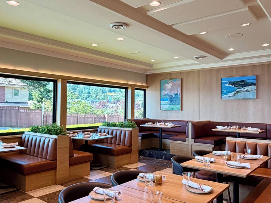 A restaurant with booths and tables, large windows, and a view of greenery.