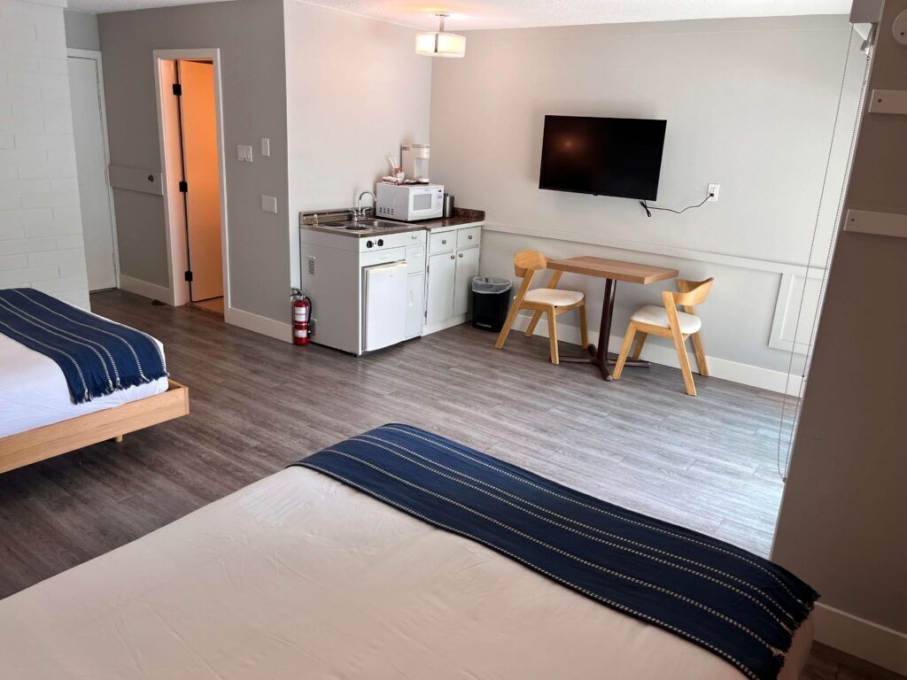 Habitación de hotel con cama, escritorio con silla, televisor, microondas y una pequeña kitchenette.