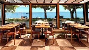 A dining area with tables and chairs, large windows with a view of the sea and a ship, and a checkered floor. - Sechelt Inn (Sechelt)