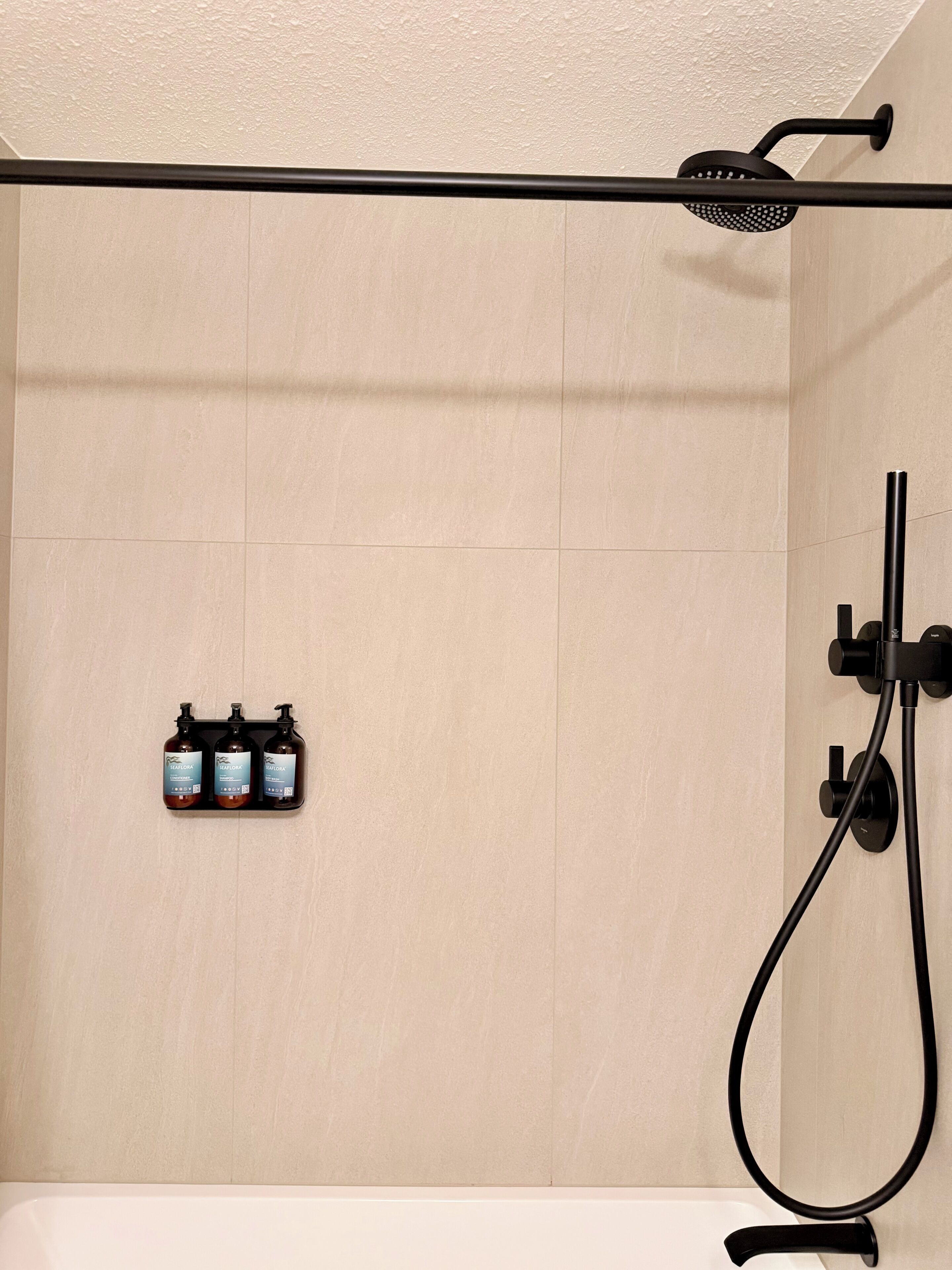 Zona de ducha con cabezal de ducha manual y tres botellas de gel de baño Seafora.
