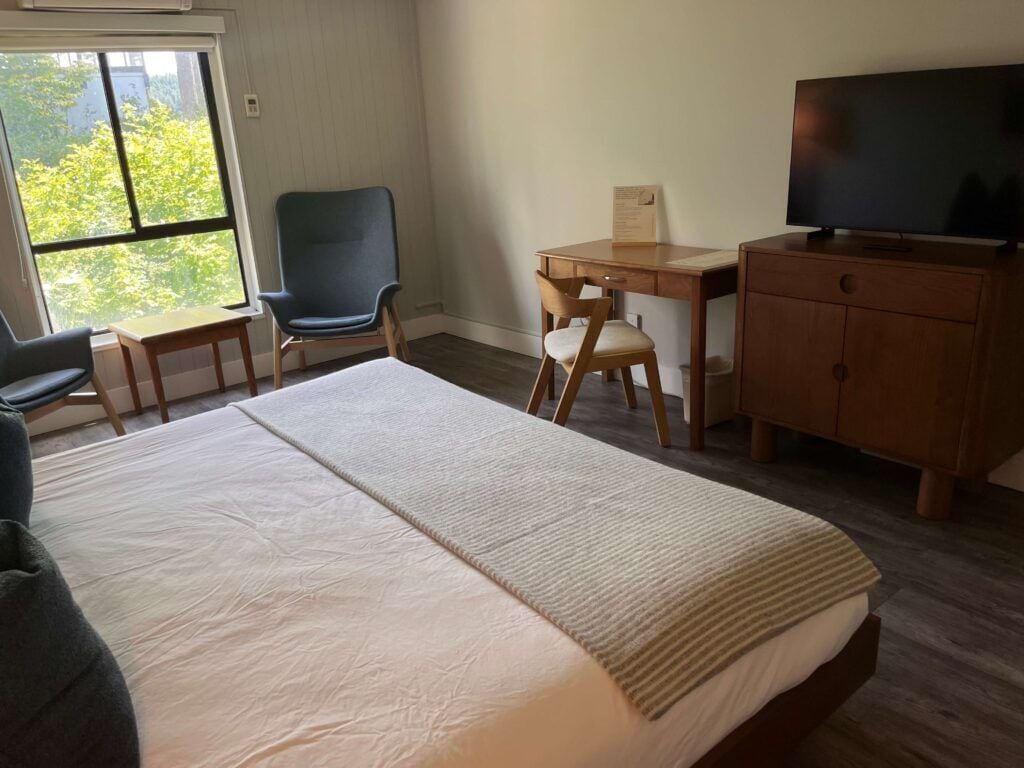 Une chambre d’hôtel avec un grand lit, un bureau, une chaise, une télévision et une fenêtre donnant sur la verdure.