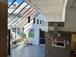 Een modern interieur met een glazen dak, een groene stoel, een klein tafeltje en een klok aan de muur.