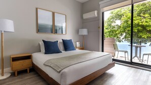 A modern bedroom with a large bed, two nightstands, a window with a view of the sea, and a balcony with outdoor seating. - Sechelt Inn (Sechelt)