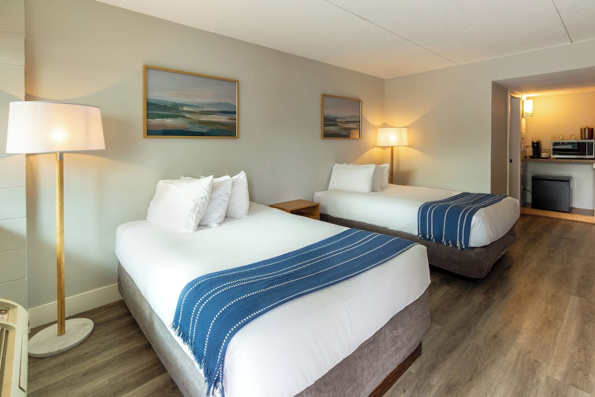 A hotel room with two beds, a small kitchenette, and a view of the outdoors.
