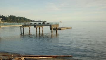 A pier extending into calm water with a bridge in the background and a forested hillside.