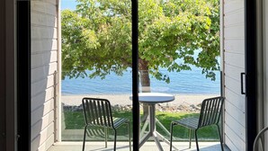 A room with a sliding glass door leading to a balcony with a table and two chairs, overlooking a body of water and greenery. - Sechelt Inn (Sechelt)