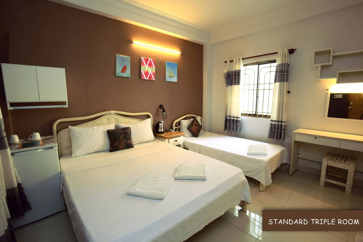 Quarto triplo standard com duas camas de solteiro, uma escrivaninha, uma mesinha e um guarda-roupa.