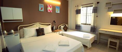 A standard triple room with two single beds, a desk, a small table, and a wardrobe.