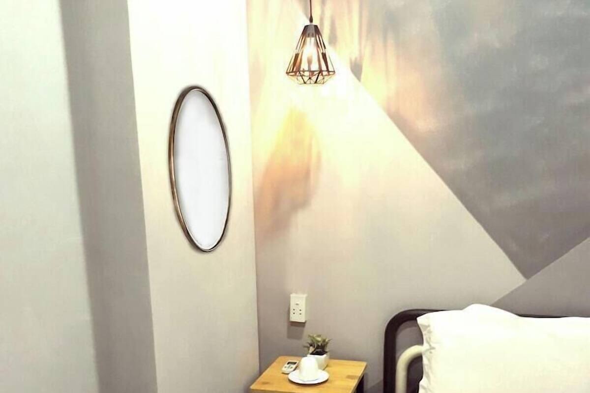 Quarto de hotel com uma cama, uma mesa de cabeceira com abajur, uma pequena planta e um candeeiro fixado na parede.
