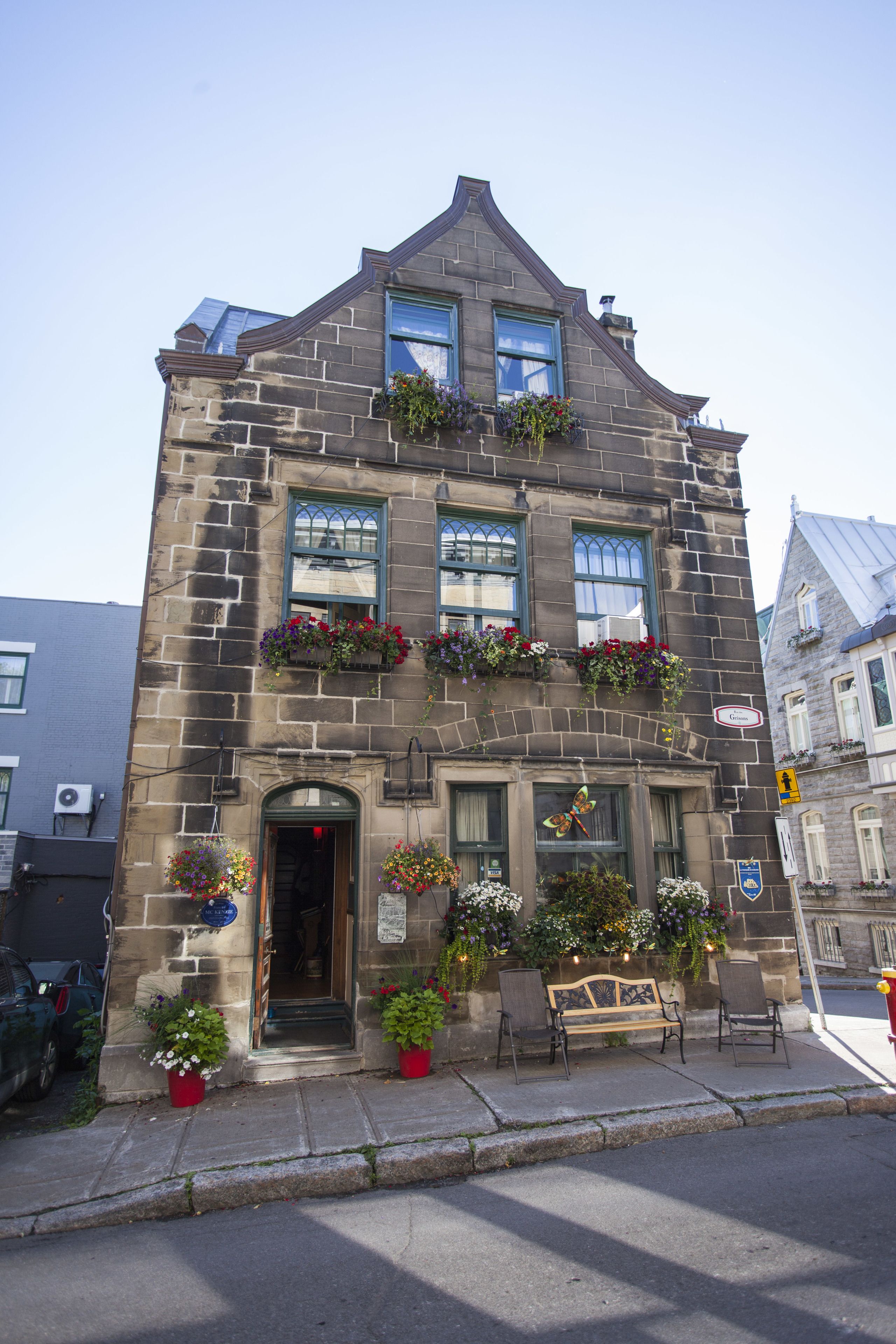 Ein Gebäude aus Stein mit vielen Fenstern, Blumenkästen und einer Bank vor der Fassade.