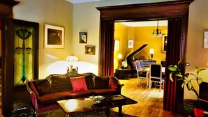 A living room with a sofa, coffee table, and a piano in the background. - B&B La Marquise de Bassano / B&B Québec (Québec City)