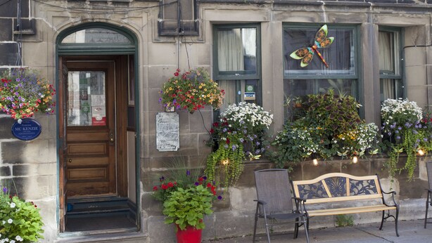 A building with a stone facade, multiple windows with flower boxes, a wooden door, and a bench outside. - B&B La Marquise de Bassano / B&B Québec (Québec City)