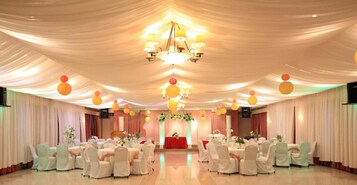 Un salón de banquetes con mesas redondas, sillas blancas y un candelabro.